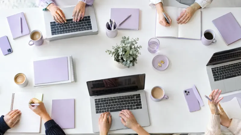 Overhead view of a shared desk with laptops and notebooks as several people work together, an SEO agency team at work