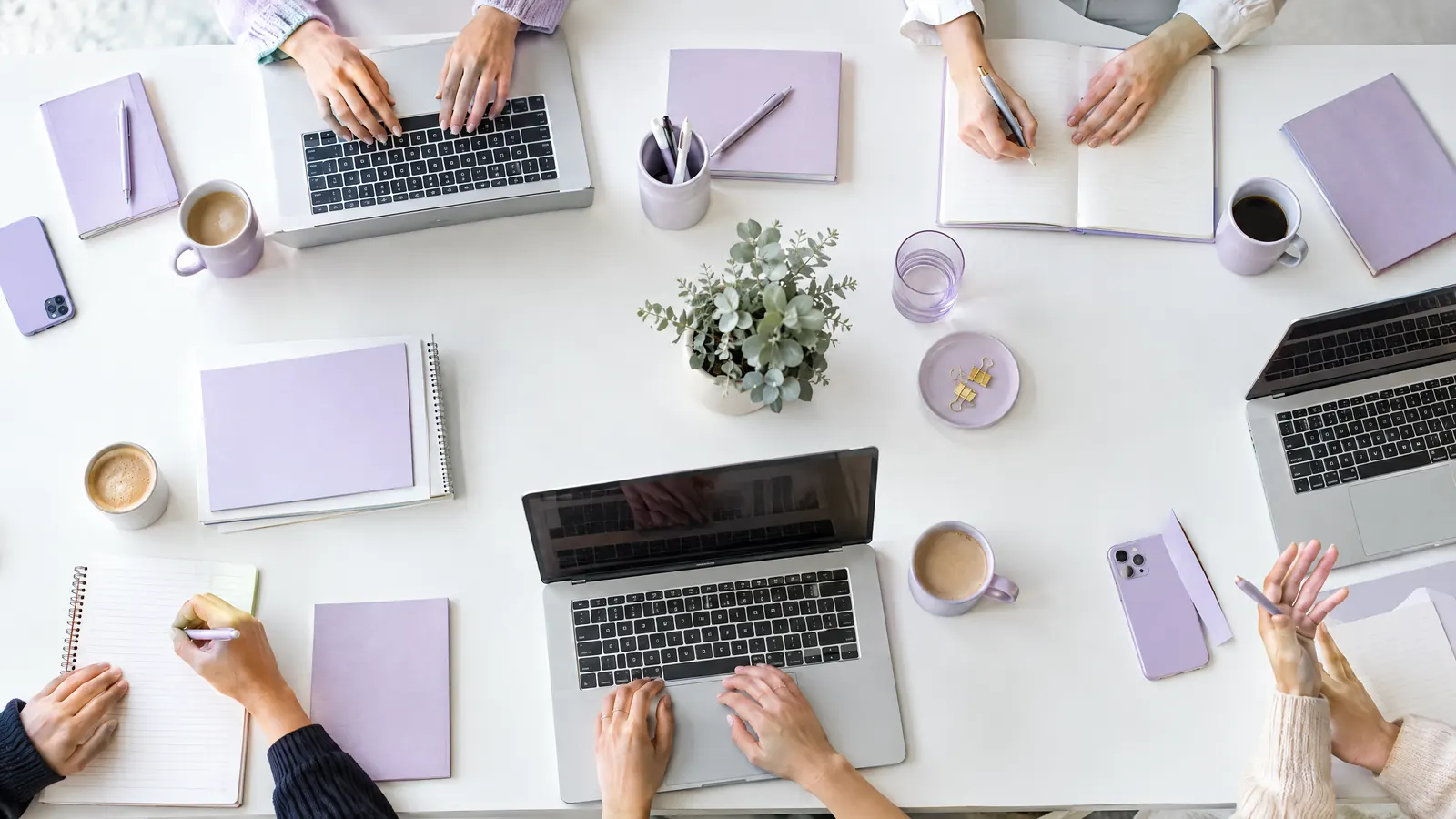 Overhead view of a shared desk with laptops and notebooks as several people work together, an SEO agency team at work